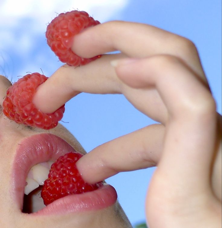 a person holding raspberries in their mouth with one hand on the other side