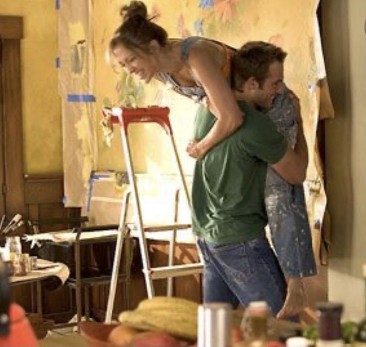 a man and woman standing next to each other in a room filled with clutter