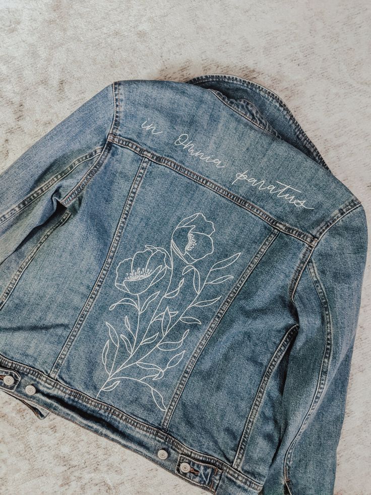 the back of a jean jacket with embroidered flowers and words on it, sitting on a carpet