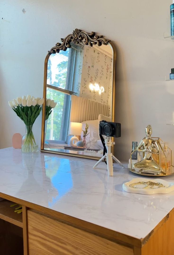 a mirror sitting on top of a counter next to a vase with flowers in it