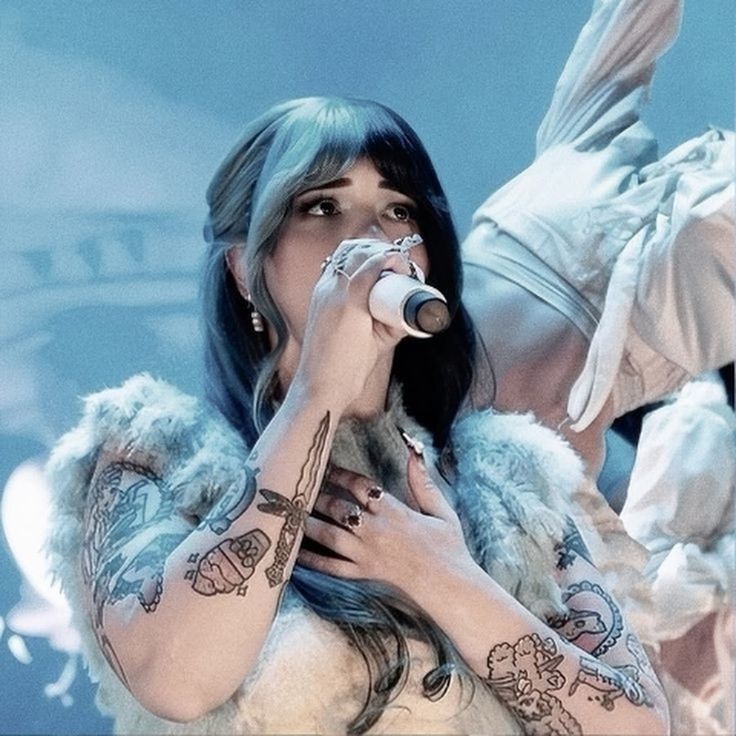 a woman with tattoos on her arms holding a microphone in front of her face and wings