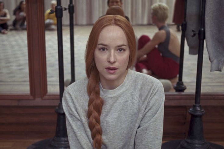 a woman with long red hair sitting in front of a mirror and looking at the camera