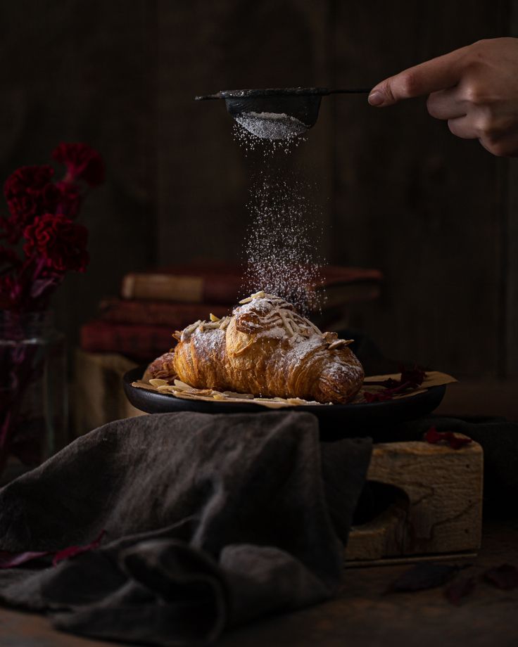 a person is sprinkling sugar on a croissant