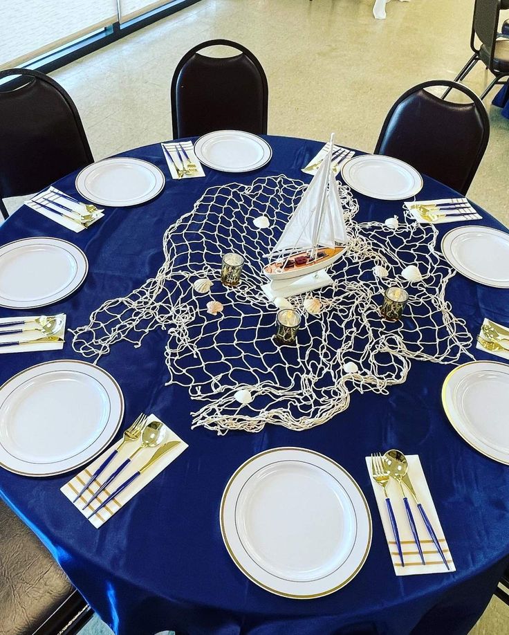 a table set with plates, silverware and a sailboat decoration on the blue cloth