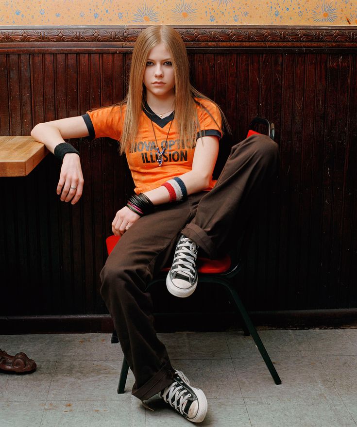 a woman sitting on a chair next to a man in an orange shirt and brown pants