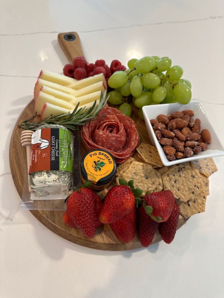 an assortment of cheeses, crackers, strawberries and grapes on a wooden platter