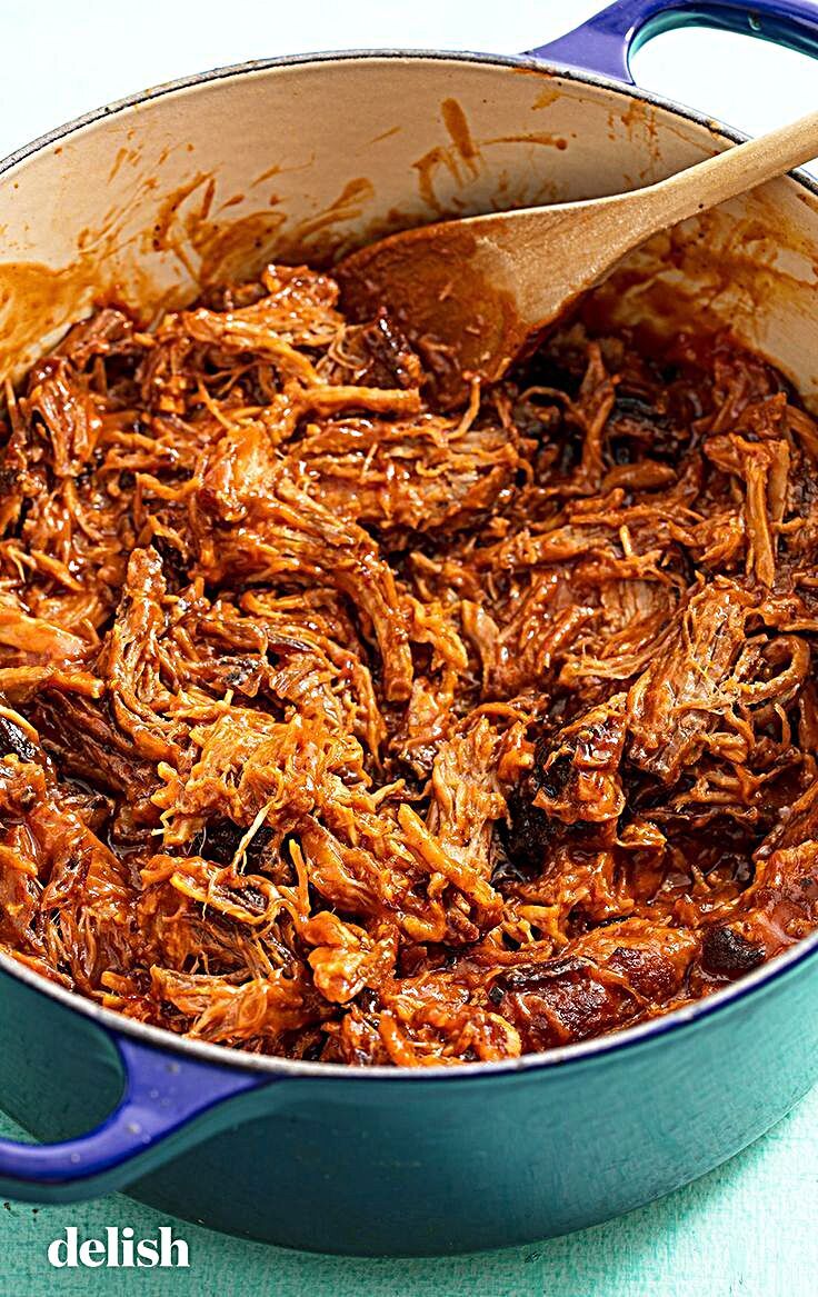 shredded pulled pork in a blue pot with a wooden ladle on the side, ready to be eaten