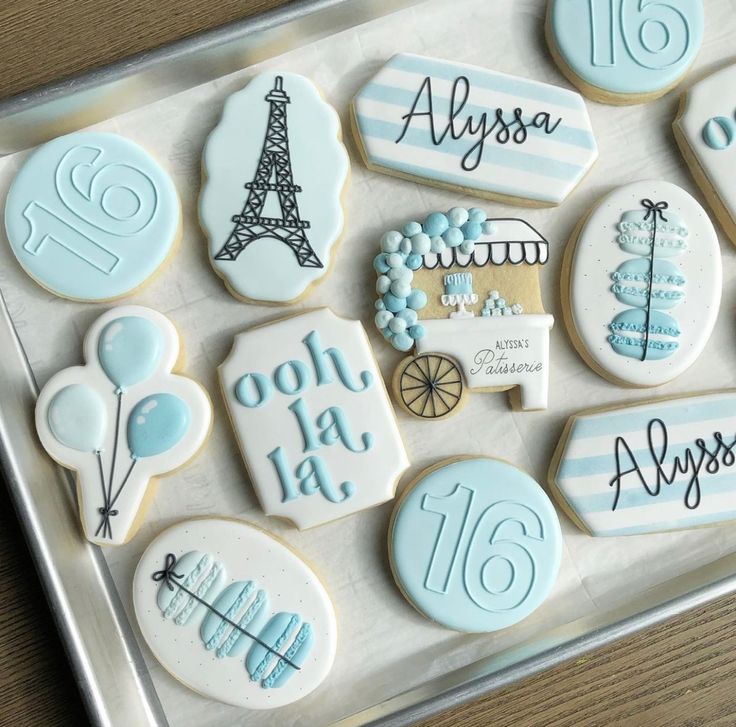 cookies decorated with blue and white icing are displayed on a tray in front of the eiffel tower