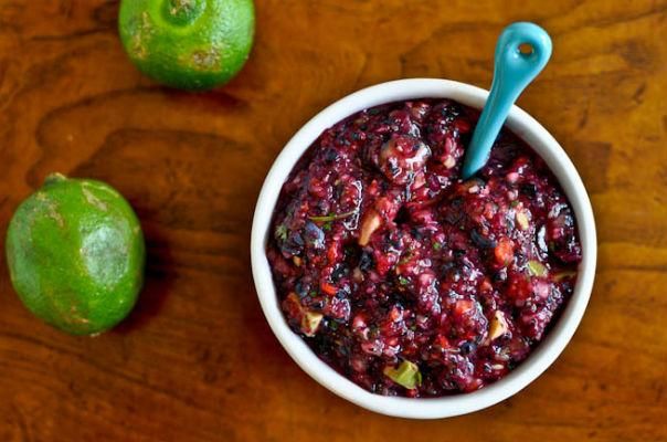 a white bowl filled with cranberry sauce next to an apple on a wooden table