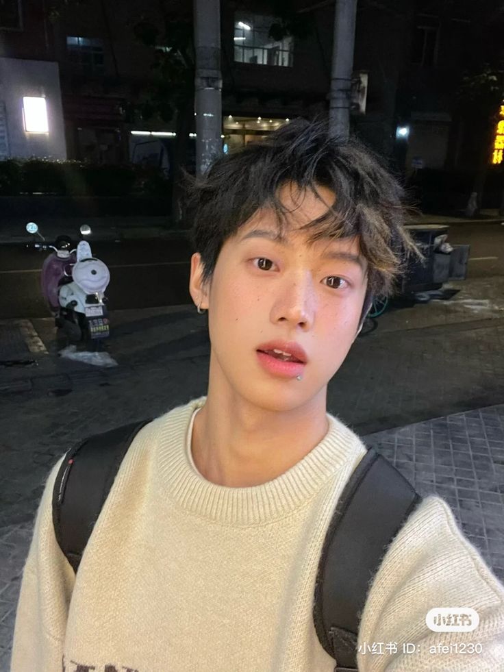 a young man standing on the street at night with his backpack over his shoulder and looking into the camera