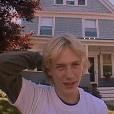 a young man standing in front of a house with his hands on his head and looking at the camera