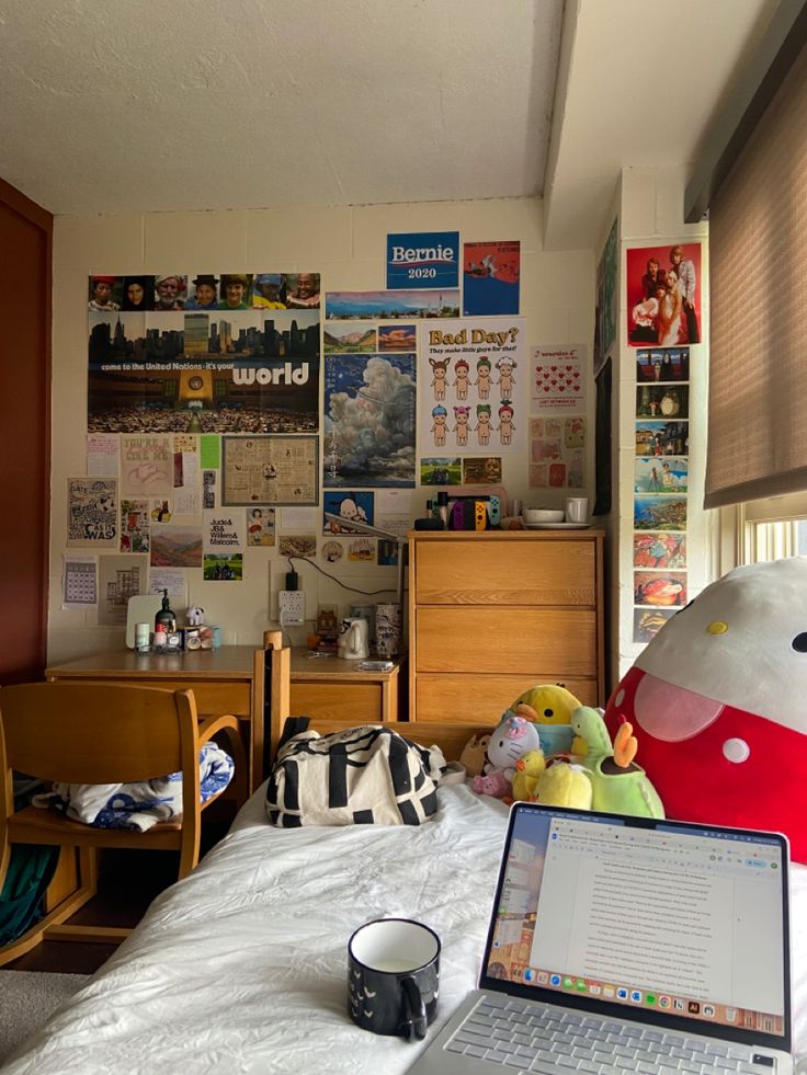 a laptop computer sitting on top of a bed next to a desk with a stuffed animal