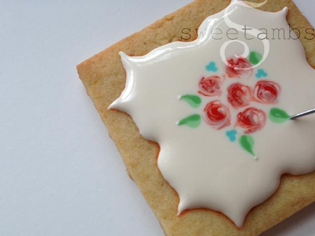 a cookie decorated with white icing and red roses on it is being held by a pair of scissors