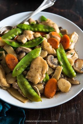 a white plate topped with chicken and veggies on top of a wooden table