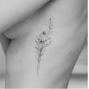 a small flower tattoo on the back of a woman's right side ribcage