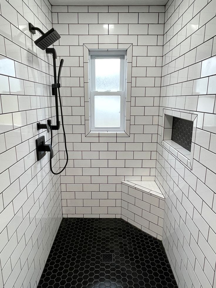 a bathroom with black and white tiles on the floor, shower head, and window