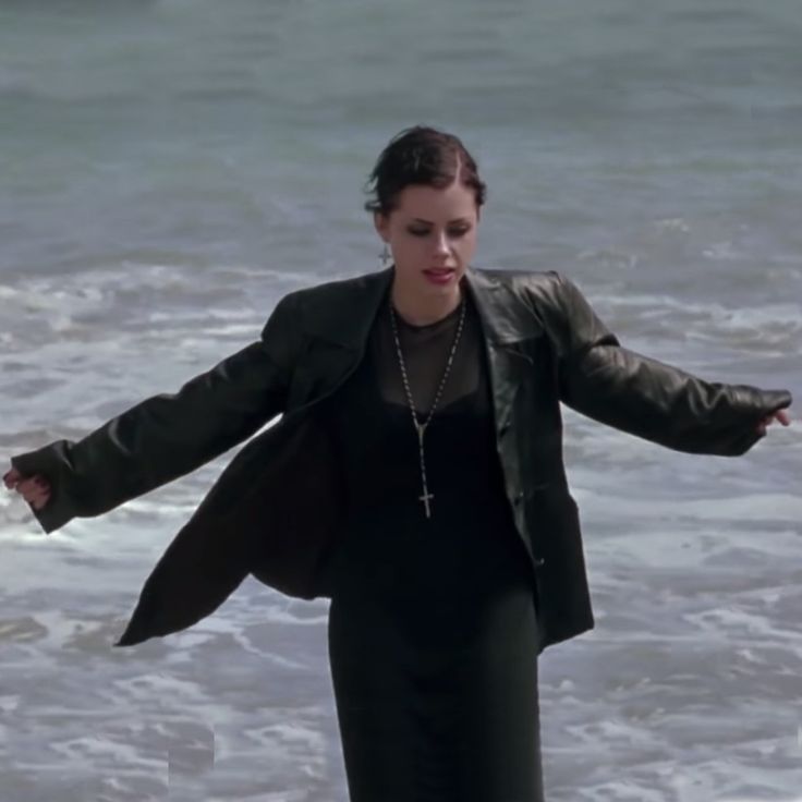 a woman standing on top of a beach next to the ocean holding her arms out