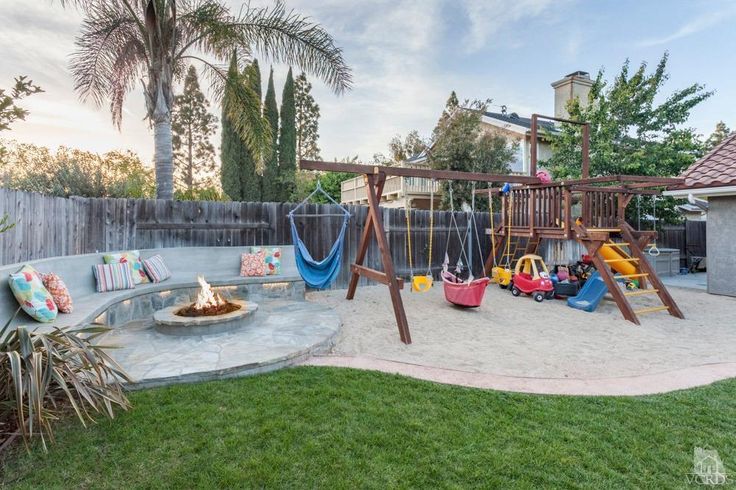 a backyard with a swing set, sand pit and fire pit in the middle of it