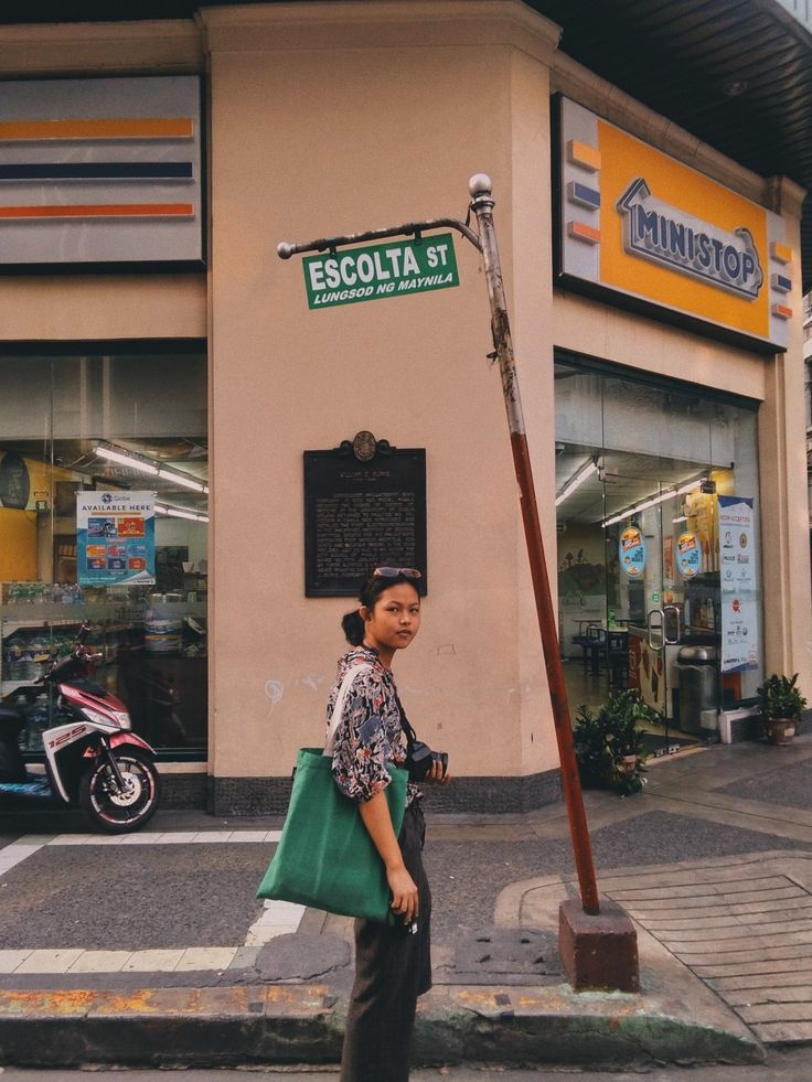 a woman walking down the street with a green bag on her shoulder and a pole in front of her