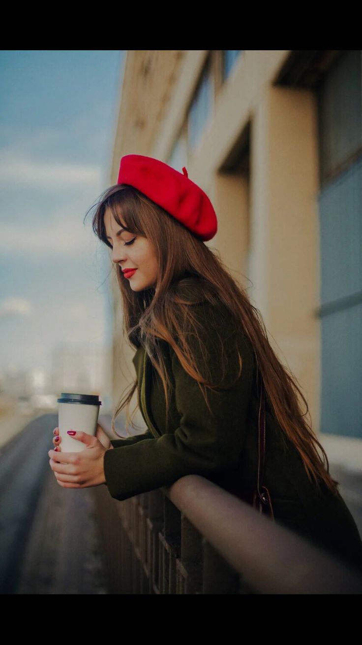 a woman with long hair holding a coffee cup and looking down at the ground while wearing a red beret