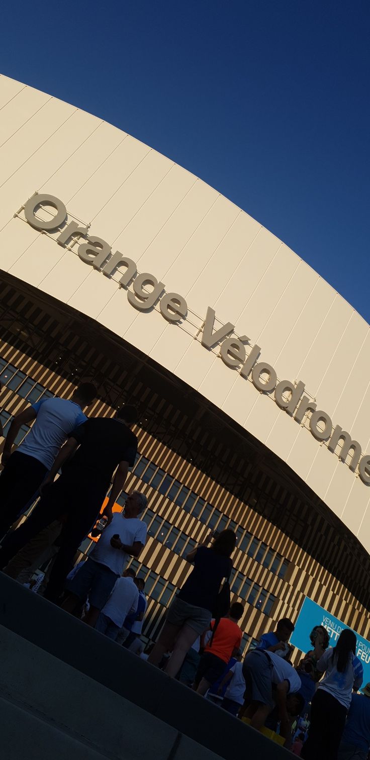 people are standing outside the entrance to an orange yellow and white building with a clock on it