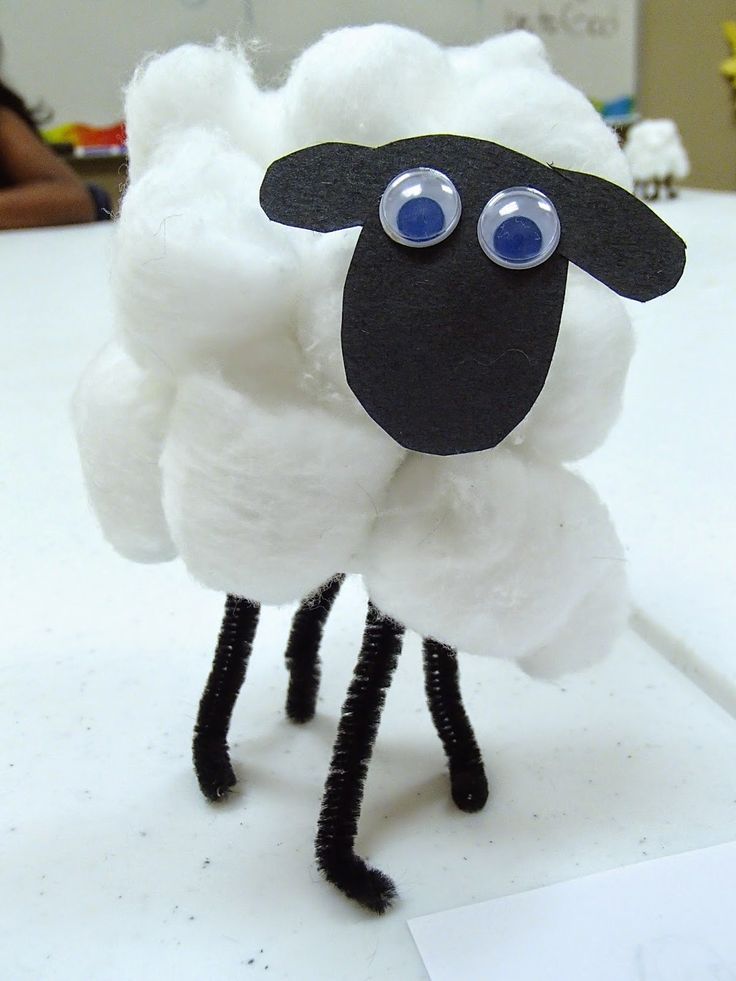 a white sheep with blue eyes and black legs standing on top of a table next to a piece of paper