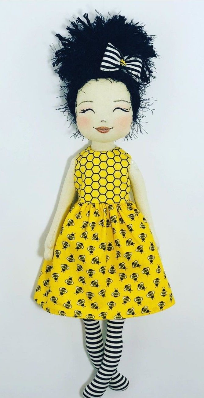 a doll with black hair wearing a yellow dress and striped socks is standing in front of a white wall