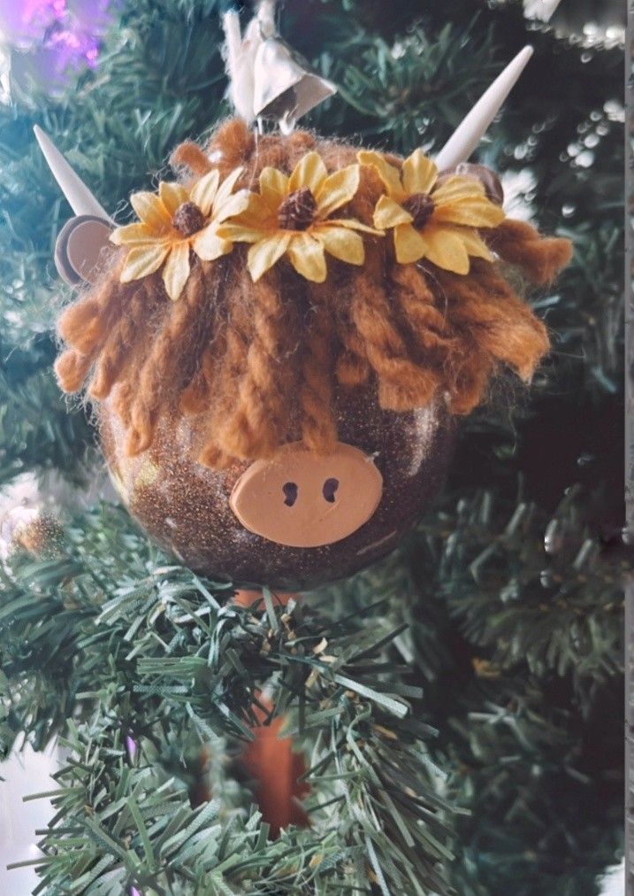 an ornament hanging from a christmas tree decorated with flowers and a cow head