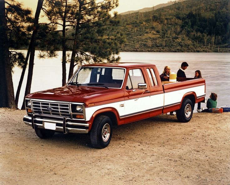 people are sitting in the bed of a red and white pickup truck by a lake