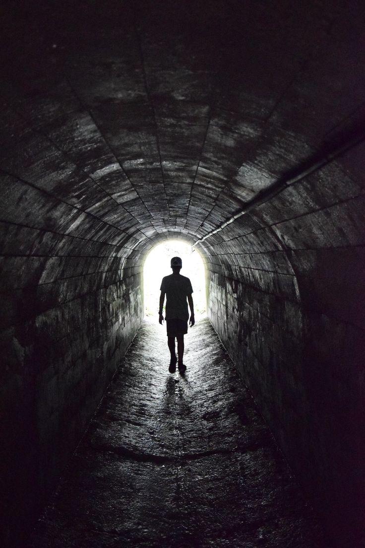 a man walking into a dark tunnel with light at the end