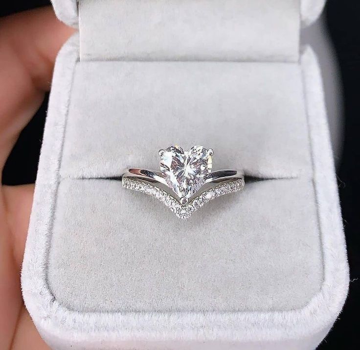 a person holding a ring with a heart shaped diamond on it's side in a velvet box