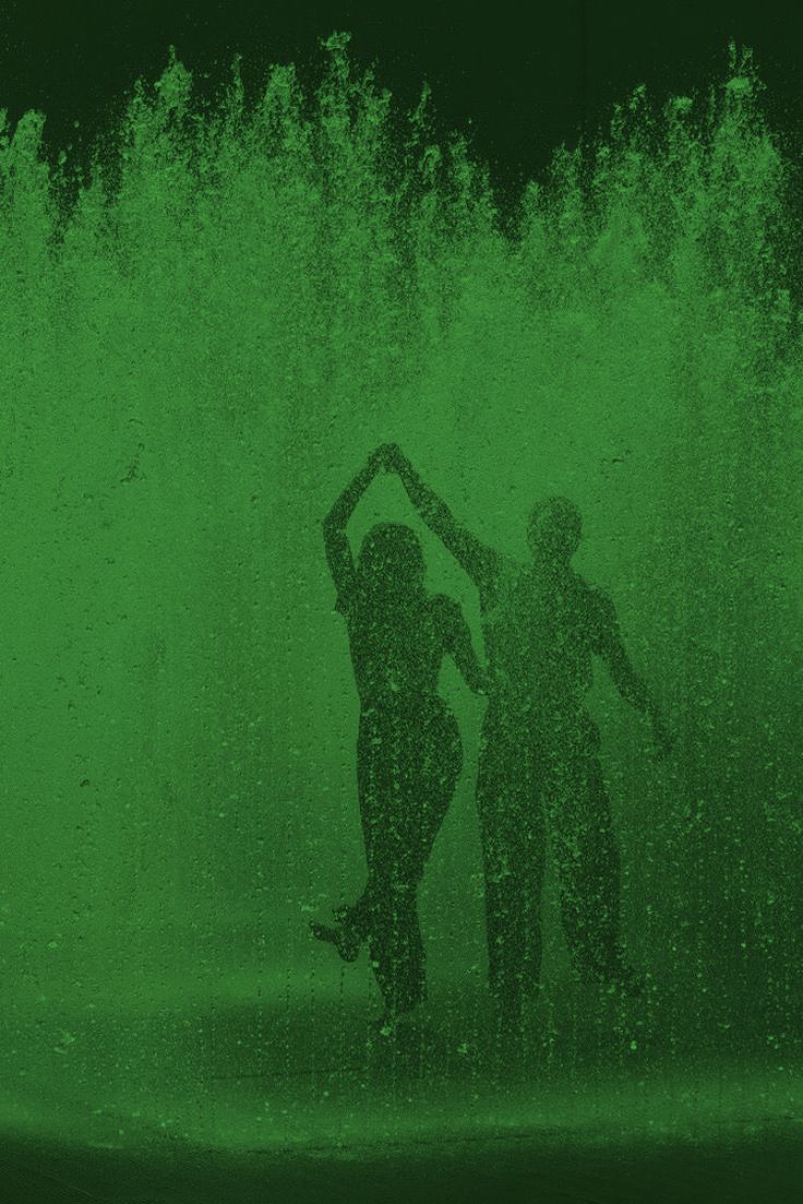 two people standing in front of a water fountain with green light coming from behind them