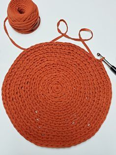 an orange round rug next to a pair of scissors and yarn on a white surface