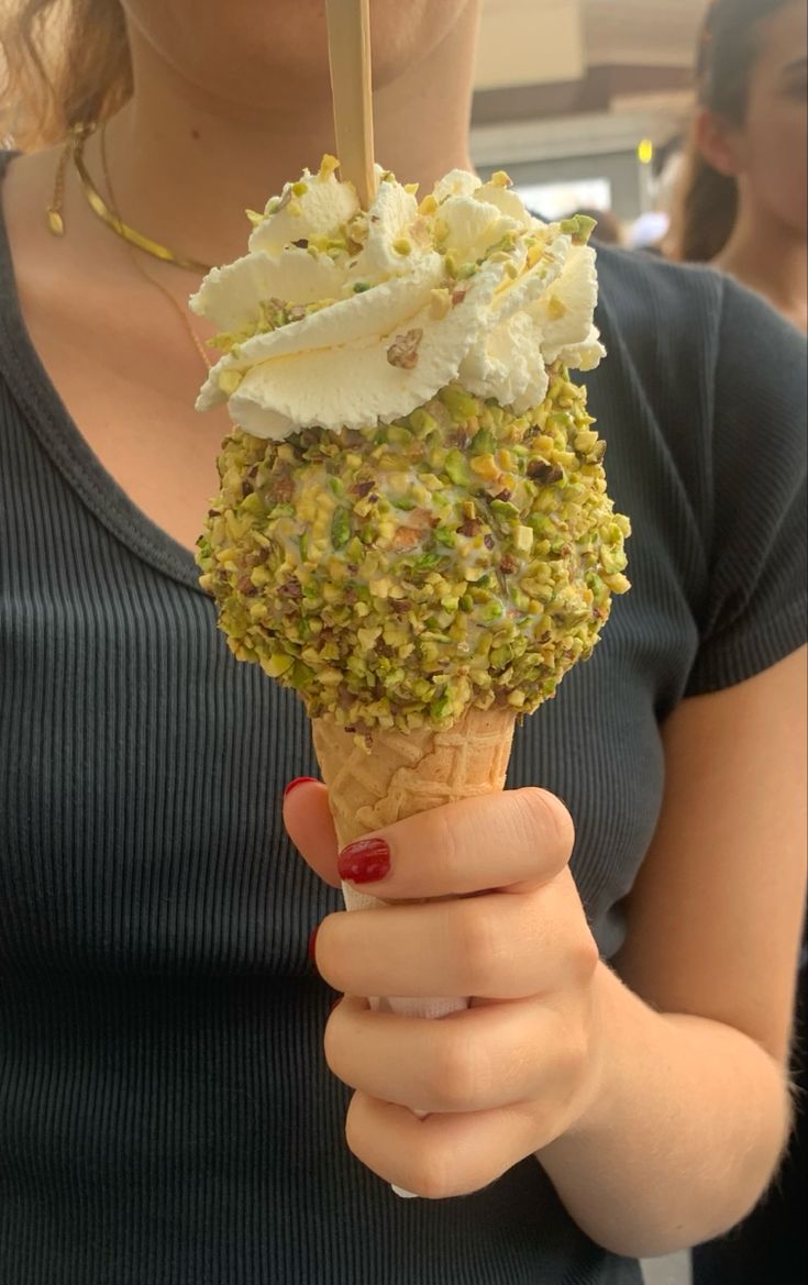 a woman is holding an ice cream cone with pistachio sprinkles