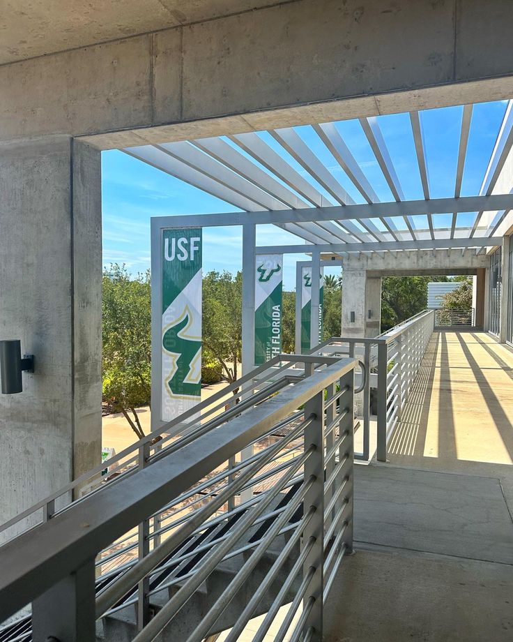 a walkway with metal railings leading to the usf and trees in the background