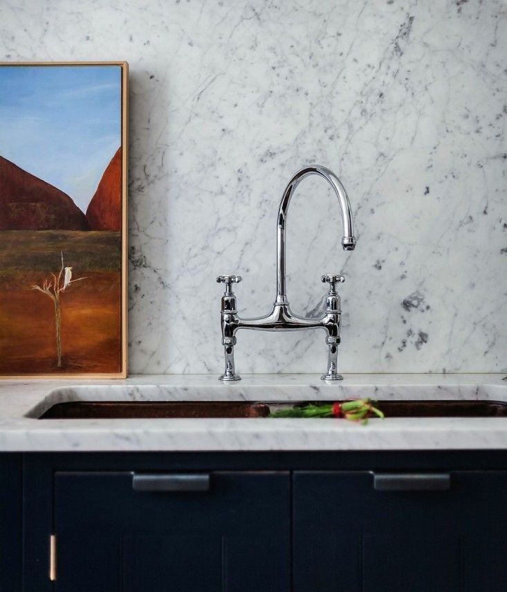 a painting hangs on the wall next to a kitchen sink with marble countertops and black cabinets