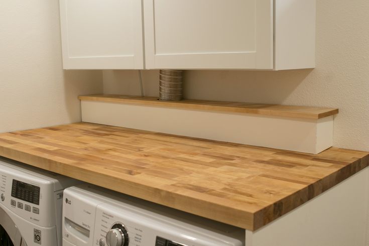 a wooden counter top next to a washer and dryer in a room with white cabinets