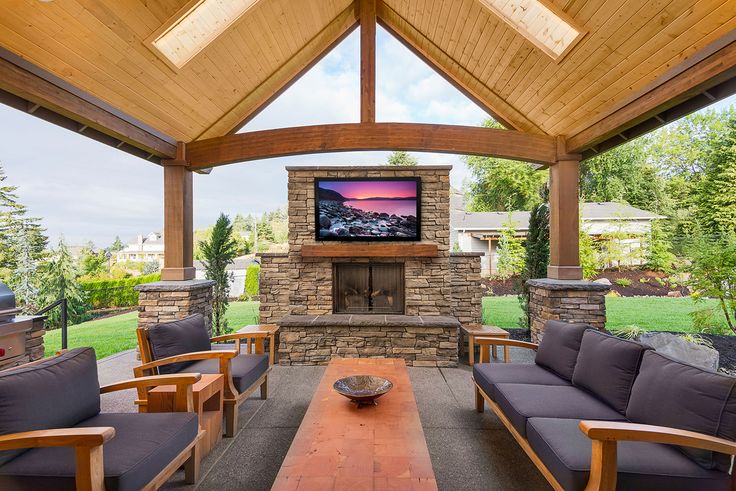 an outdoor living area with couches, tables and a television on the wall above it