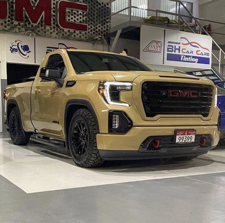 a yellow gmc truck is parked in a showroom with other vehicles behind it