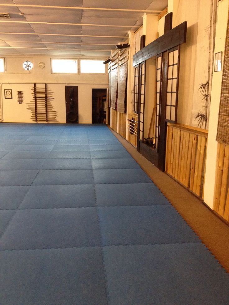 an empty gym room with blue mats on the floor and wooden doors leading to other rooms