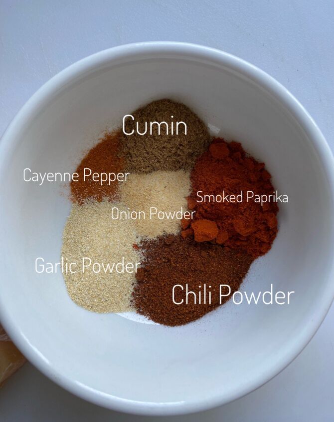 spices in a white bowl labeled with the ingredients for cumin, cayenme pepper, onion powder, and chili powder