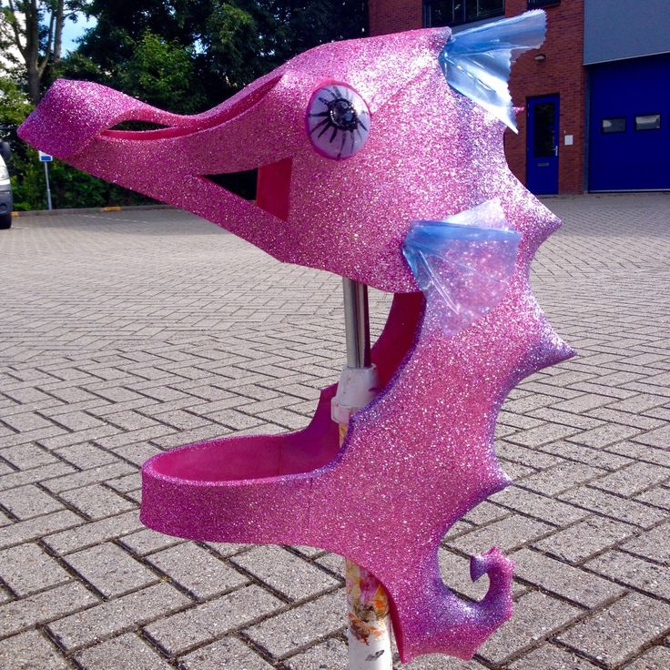 a pink plastic toy horse on top of a metal pole in front of a building