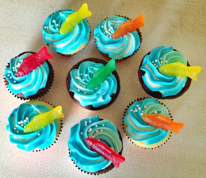 six cupcakes with blue frosting and colorful fish on them are arranged in a circle