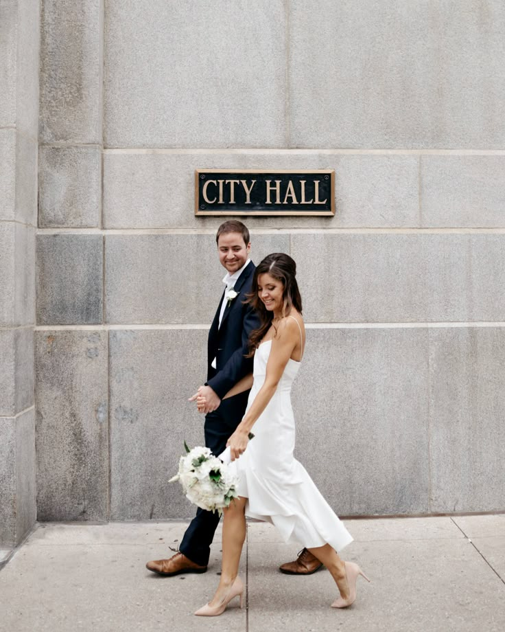 a bride and groom pose in front of the city hall sign