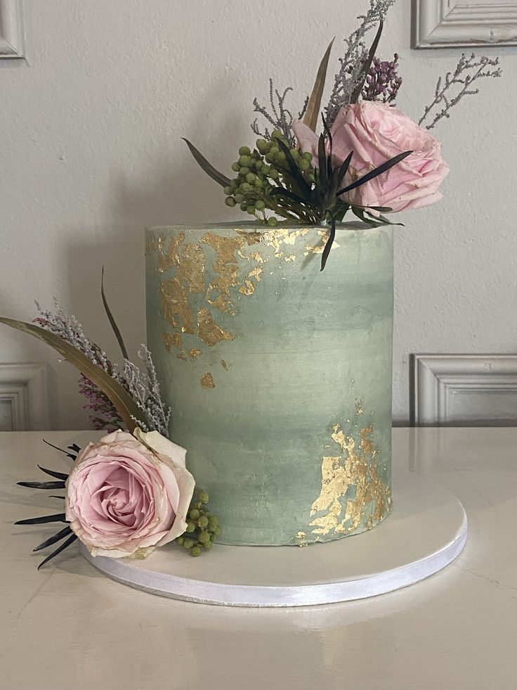 there is a green and gold cake with flowers on the top, sitting on a table