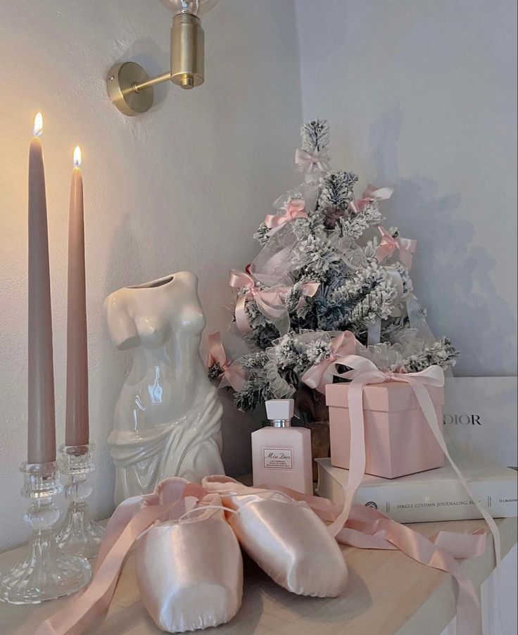 a white christmas tree with pink ribbon and candles next to it on top of a table