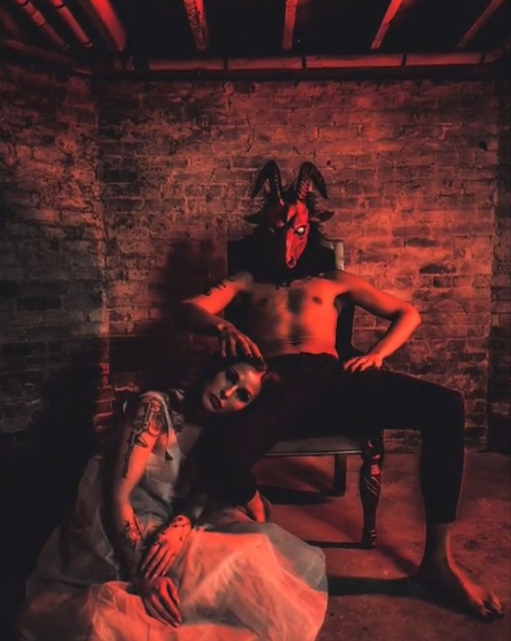 a man laying on top of a chair next to a woman in a mask and dress