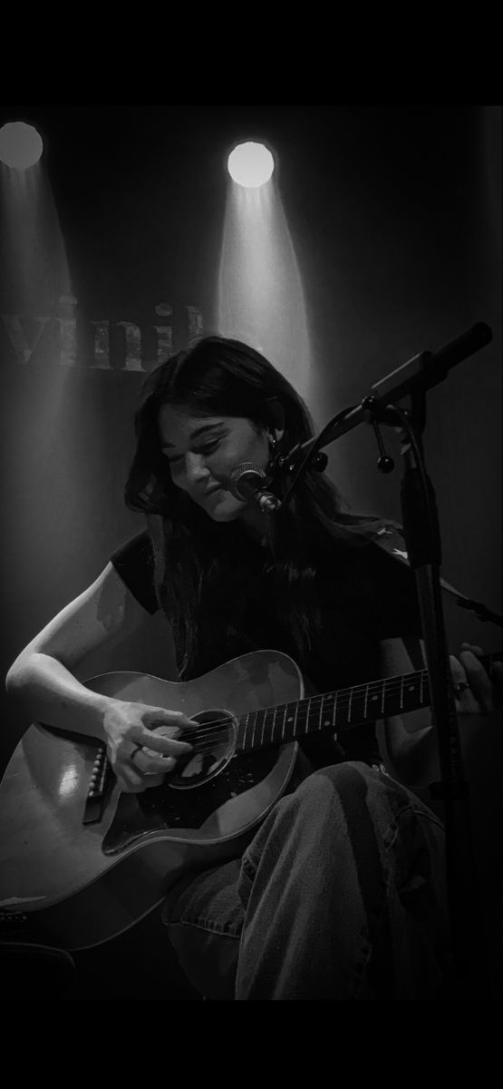 a woman sitting in front of a microphone playing a guitar