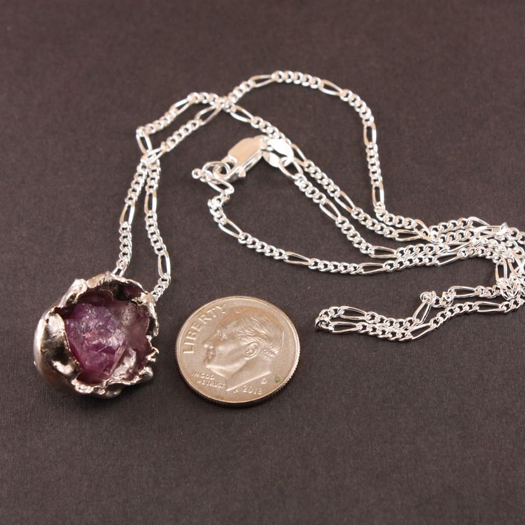 "Add a touch of whimsy to your look with our Raw Ruby and Silver Necklace. Handcrafted with water cast silver and adorned with raw ruby, this sterling silver necklace is the perfect blend of elegance and playfulness." Sterling Silver Raw Ruby Gemstone 18" Sterling Silver Chain Silver Hand Cast Round Pendant Necklace, Sterling Silver Pendant With Raw Stone, Sterling Silver Birthstone Necklaces For Healing, Healing Sterling Silver Birthstone Necklace, Silver Pendant With Raw Stone, Silver Raw Stone Pendant Jewelry, Nickel-free Sterling Silver Pendant Crystal Necklace, Raw Stone Silver Pendant Jewelry, Silver Pendant Birthstone Necklace With Natural Stones