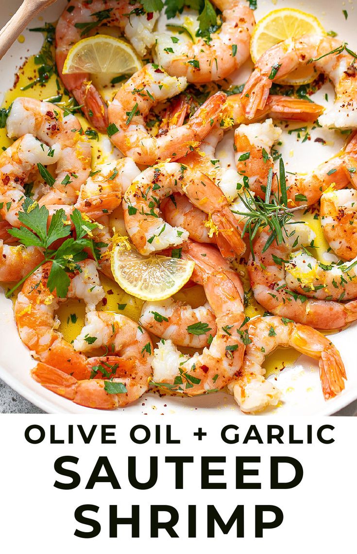 a white plate topped with shrimp next to lemon wedges and garnished with herbs